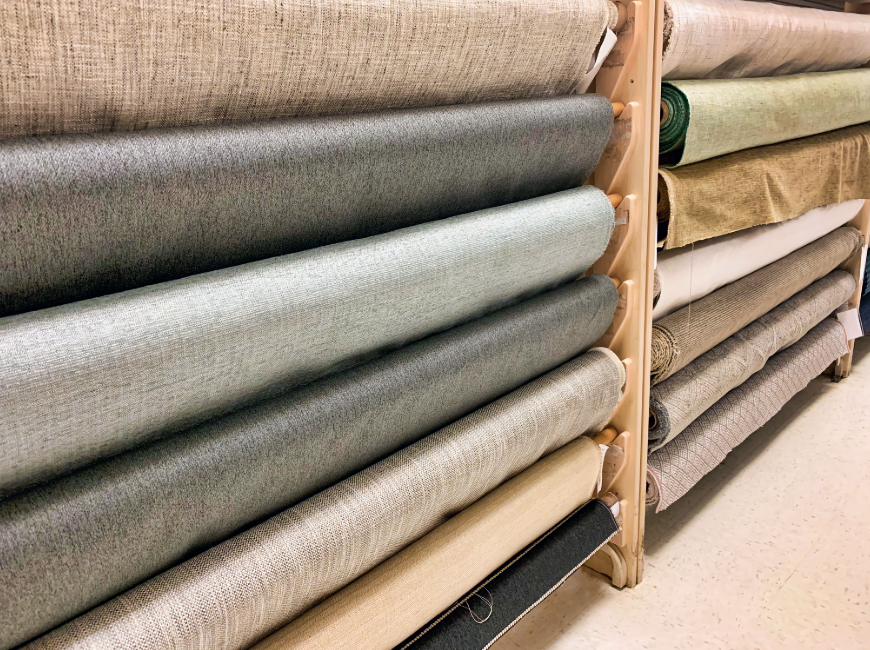 Rolls of fabric stacked on a wooden rack in a store setting
